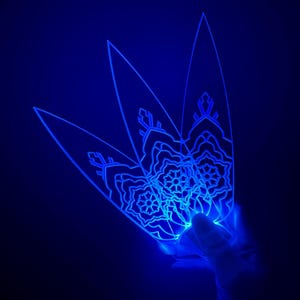 Puede incluir: Una lámpara decorativa azul brillante con un diseño floral. La lámpara se sostiene en una mano y emite una luz brillante sobre un fondo oscuro. El diseño presenta patrones intrincados.