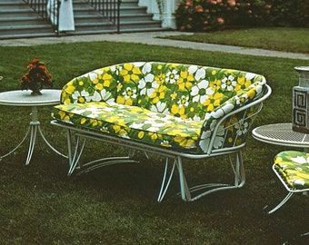 May include: A vintage outdoor seating set featuring a white metal frame and cushions with a floral pattern in green, yellow, and white. Includes a loveseat, a small side table, and a matching chair, all on a grassy lawn.