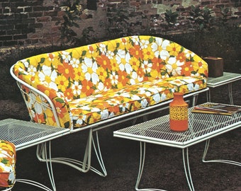May include: Outdoor patio furniture set featuring a white metal frame sofa and side tables. The sofa and cushions have a vibrant floral pattern in yellow, orange, and white. The tables have a wire mesh top. A decorative orange vase sits on a table.