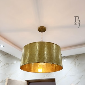May include: A gold pendant light fixture with a textured, drum-shaped shade. The shade is made of a hammered metal and has a warm, golden finish.