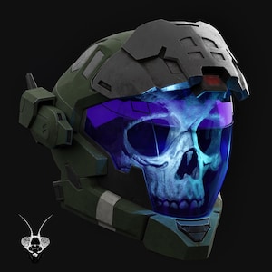 Può includere: Un casco futuristico verde scuro e nero con una visiera viola. La visiera mostra una grafica a teschio. Il casco ha un design complesso con pannelli angolari e una finitura strutturata, che suggerisce un tema fantascientifico o di gioco.