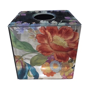 May include: A clear, square tissue box with a floral design. The box features a large, red and orange flower with green leaves, and smaller flowers in shades of blue, purple, and yellow. The top has a circular opening for tissue dispensing.