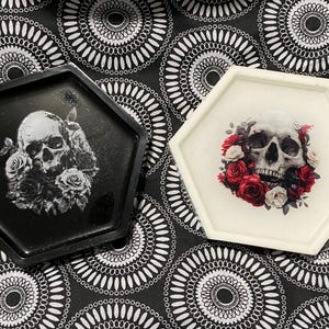 May include: Two hexagonal resin trays with a skull and floral design. One tray is black with a white skull and the other is white with a red and white skull.