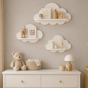 Peut inclure: Trois étagères murales blanches en forme de nuage portant de petits objets décoratifs, dont un panneau indiquant Twinkle Little Star et un autre I Love You To The Moon And Back, au-dessus d'une commode blanche à six tiroirs avec des boutons en bois.