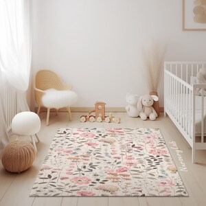 May include: A rectangular rug with a floral pattern in pink, beige, and gray tones. The rug features a variety of flowers and leaves, creating a soft and inviting look. The rug is placed in a nursery setting, with a crib and toys visible.