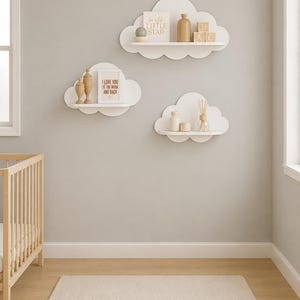 May include: Three white cloud-shaped wall shelves mounted on a wall. The top shelf holds a sign reading "twinkle LITTLE STAR", a tan bottle, and wooden blocks. The left shelf holds two wooden finials and a sign reading "I LOVE YOU TO THE MOON AND BACK". The bottom shelf holds two small jars and a reed diffuser.