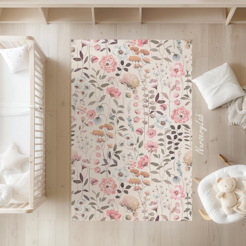 May include: A rectangular rug with a floral pattern featuring pink, peach, and blue flowers on a cream background. The rug is surrounded by light-colored wooden flooring and a crib.