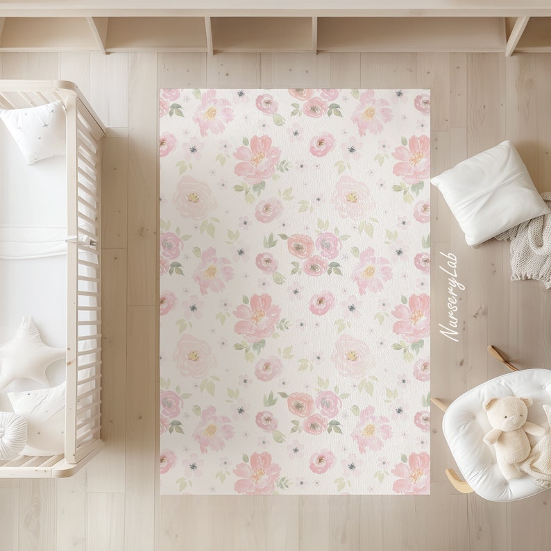 May include: A rectangular rug with a floral pattern of pink roses and green leaves on a cream background. The rug is in a nursery setting, with a crib and rocking chair visible. The text "Nursery Lab" is on the rug.