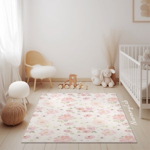 May include: A rectangular rug with a floral pattern in a nursery setting. The rug features a cream background with pink and peach-colored flowers and green leaves. The room includes a white crib, a wooden toy train, and a wicker chair.
