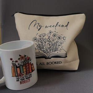 K&ouml;nnte beinhalten: Eine wei&szlig;e Keramiktasse mit einem Blumendesign und dem Text "Es gibt kein solches Ding wie zu viele B&uuml;cher". Eine wei&szlig;e Stofftasche mit dem Text "Mein Wochenende ist ausgebucht" und einem Blumendesign.