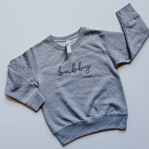 May include: Grey sweatshirt with the word "bubby" embroidered in black cursive lettering.