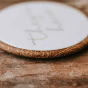 May include: Close-up of a round wooden embroidery hoop with a white fabric center. The fabric has the word "Thank you" written in cursive on it.