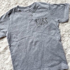 May include: A gray short-sleeved t-shirt with the word "BUBS" embroidered on the front in black thread.