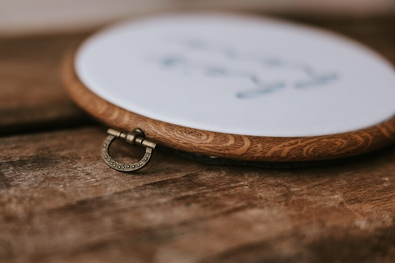 May include: A wooden embroidery hoop with a white fabric stretched across it. The hoop has a brass latch on the side.