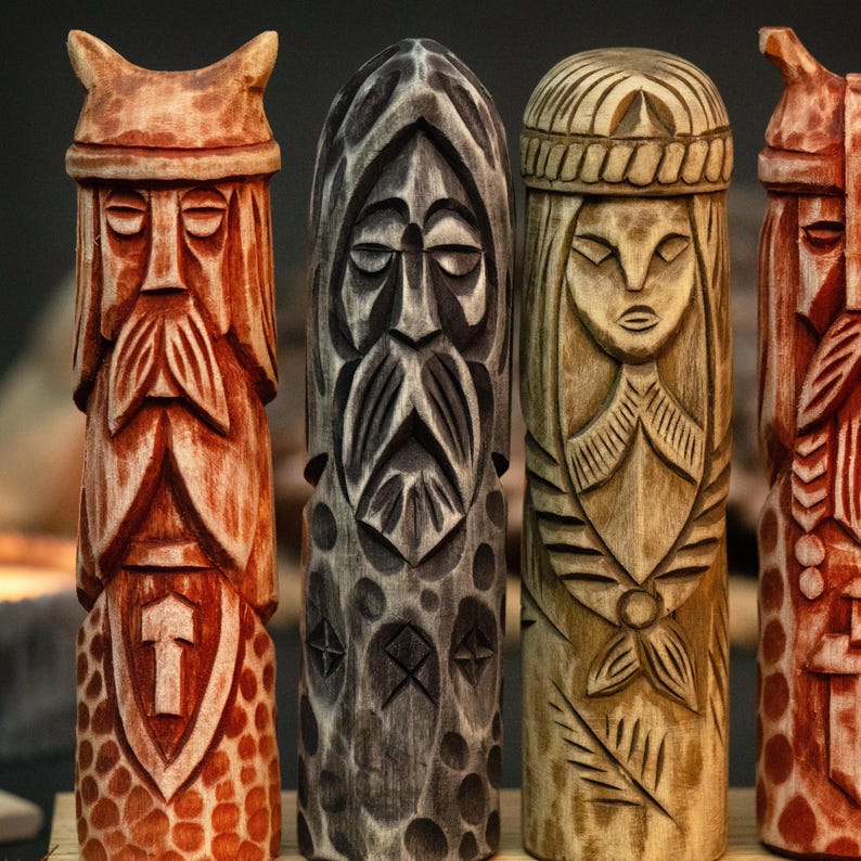 May include: Four intricately carved wooden statues. The statues are of various colors, including reddish-brown, gray, and light brown. Each statue has a unique design, depicting faces and patterns. The carvings appear to be of a historical or cultural theme.