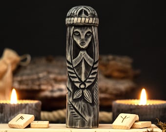 May include: A carved wooden statue of a woman with a crown, featuring intricate details and a weathered gray finish. The statue is displayed with wooden runes and lit candles, creating a mystical ambiance.