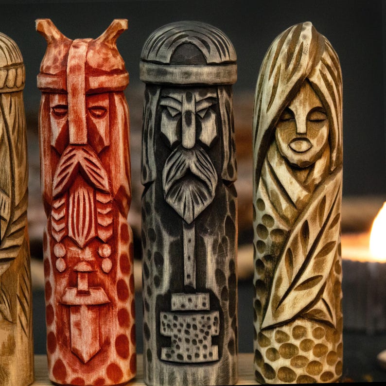 May include: Close-up of four carved wooden figures. The figures are in shades of red, gray, and tan. Each figure has a detailed face and is carved with intricate patterns. The figures appear to be of a religious or mythological theme.