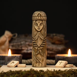 May include: A carved wooden statue of a woman with intricate details, including a headdress and facial features. The statue is displayed on a wooden base with runes and lit candles in the background, creating a mystical ambiance.