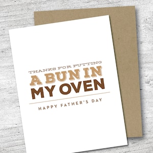 May include: A white Father's Day card with the text "THANKS FOR PUTTING A BUN IN MY OVEN" in brown lettering. The card is paired with a brown envelope. The words "HAPPY FATHER'S DAY" are printed at the bottom.