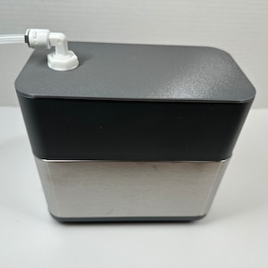 Op de afbeelding: Een waterdispenser van roestvrij staal en grijs met een witte kunststof slang en een witte kunststof connector.