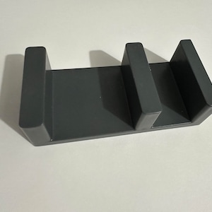 May include: A dark gray plastic organizer with three slots for holding items. The organizer is made of a sturdy material and has a sleek, modern design.