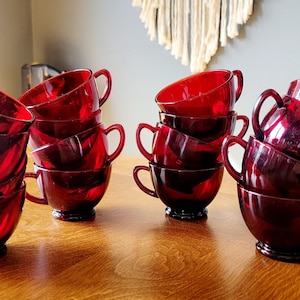 May include: A set of 12 ruby red glass teacups stacked in two piles of six. The cups are all the same size and shape, and they have a classic design.