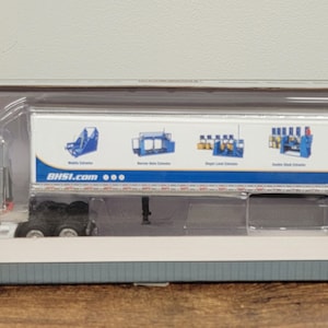 May include: A white diecast model of a semi-truck and trailer with the logo "Mobil" and the website "mobil.com" on the side of the trailer. The trailer has images of shelves with various products on it.