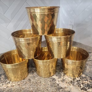 May include: Six gold-colored metal planters with a hammered finish. The planters are stacked in a pyramid shape.