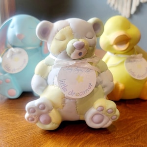 May include: Three ceramic figurines of a blue bunny, a yellow duck, and a patchwork bear. Each figurine has a round tag that says "little dreamer" with a star in the center. The bear's tag also says "Lady Jayne Ltd."