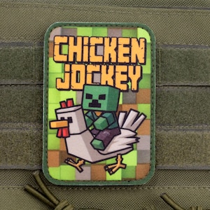 May include: A rectangular morale patch featuring a green pixelated background with the text CHICKEN JOCKEY in yellow block letters. The graphic depicts a green block-style creature riding a white chicken with a red comb and yellow feet.