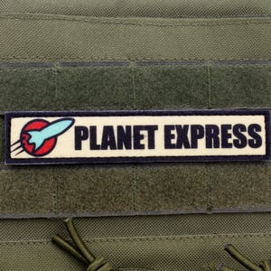 May include: A black and white patch with a blue and red rocket ship and the text "PLANET EXPRESS" on a green background.