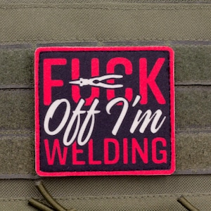 Könnte beinhalten: Ein quadratischer Aufnäher mit dem Text "FUCK Off I'm WELDING" in Rot und Weiß, mit einer Schweißwerkzeug-Grafik. Der Aufnäher hat einen schwarzen Hintergrund und einen roten Rand, befestigt an einem grünen Stoff.