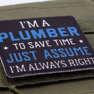 K&ouml;nnte beinhalten: Ein rechteckiger Aufn&auml;her mit dem Text "I'M A PLUMBER TO SAVE TIME JUST ASSUME I'M ALWAYS RIGHT" in wei&szlig;er und blauer Schrift. Der Aufn&auml;her ist schwarz mit wei&szlig;em Rand und vor gr&uuml;nem Hintergrund.