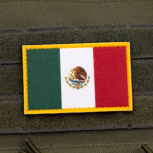 May include: A rectangular patch featuring the Mexican flag, with green, white, and red vertical stripes and the Mexican coat of arms in the center. The patch has a yellow border and is set against a textured olive-green background.