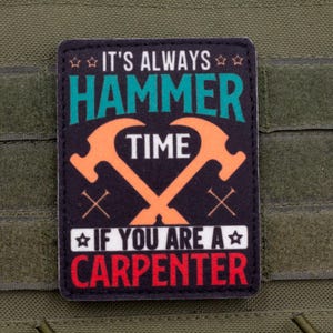 May include: A black patch with the text "IT'S ALWAYS HAMMER TIME IF YOU ARE A CARPENTER." The patch features crossed hammers in orange and white text on a green background. The patch is attached to a green fabric.