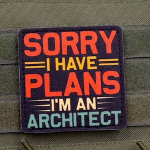 May include: A rectangular patch with the text "SORRY I HAVE PLANS I'M AN ARCHITECT" in red, yellow, and teal against a navy blue background. The patch is attached to a green fabric.