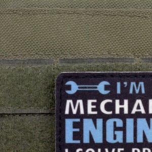 May include: Close-up of a green fabric with a patch that reads "I'M A MECHANIC ENGINEER I SOLVE PROBLEMS". The patch has a black background with white and blue text and a wrench graphic.