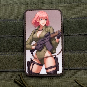 May include: A pink-haired anime character in a green jumpsuit holds a black rifle with a scope. The character is wearing black gloves and has a serious expression. The image is printed on a brown patch with a black border.