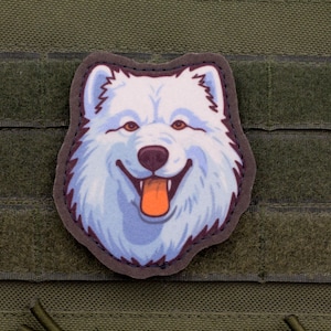 May include: A patch featuring a smiling cartoon dog with white fur, brown eyes, and an orange tongue. The patch is bordered in dark brown and is affixed to a green fabric background.