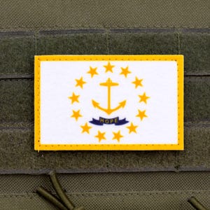 May include: A rectangular patch displaying the Rhode Island state flag. The design features a white background with a gold anchor encircled by 13 gold stars. The word "HOPE" is on a blue banner below the anchor. The patch has a yellow border.