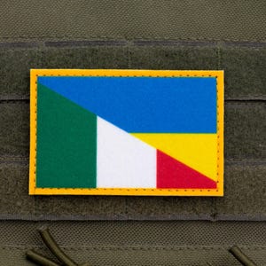 以下が含まれることがあります： イタリアとウクライナの国旗を組み合わせたデザインの、黄色の縁取りがある長方形のパッチ。 パッチは緑色の生地に付けられており、おそらくタクティカルベストです。 デザインには緑、白、赤、青、黄色が含まれています。