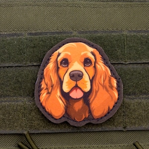 May include: A patch featuring a detailed illustration of a Cocker Spaniel dog with orange and brown fur, a black outline, and a pink tongue. The patch is affixed to a green fabric background.