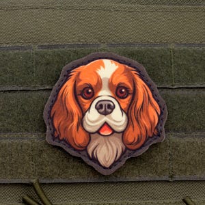 May include: A colorful patch featuring a Cavalier King Charles Spaniel dog. The patch has a detailed illustration of the dog's face, with brown, white, and orange fur, and is set against a green background.