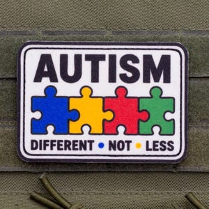 Puede incluir: Un parche rectangular con fondo blanco y borde negro. La palabra AUTISM está impresa en negro en la parte superior. Debajo, cuatro piezas de rompecabezas en azul, amarillo, rojo y verde están alineadas. El texto DIFFERENT • NOT • LESS está abajo.