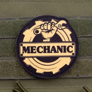 May include: A round patch with the word "MECHANIC" in a rectangular frame, set against a gear and a clenched fist holding a wrench. The patch is black and tan, and is set against a green background.