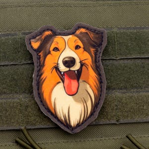 Può includere: Una toppa raffigurante un cane sorridente con pelo arancione, marrone e bianco, un naso nero e una lingua rossa. La toppa è posta su uno sfondo verde con cinghie in velcro.