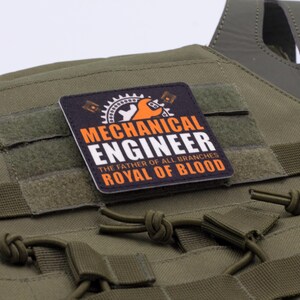 Pu&ograve; includere: Gilet tattico verde oliva con una toppa che recita "MECHANICAL ENGINEER THE FATHER OF ALL BRANCHES ROYAL OF BLOOD" in bianco e arancione. Il gilet ha pi&ugrave; cinghie e un'area con chiusura a strappo.