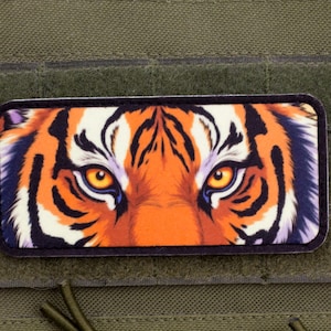 May include: A rectangular patch featuring a close-up of a tiger's face. The tiger's eyes are yellow, and the fur is orange, black, and white. The patch is set against a green background.