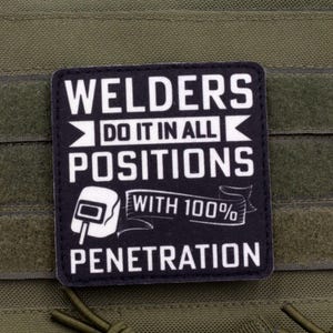 Può includere: Toppa in bianco e nero con la scritta "WELDERS DO IT IN ALL POSITIONS WITH 100% PENETRATION" e una grafica di maschera per saldatura. La toppa è su un gilet tattico verde.