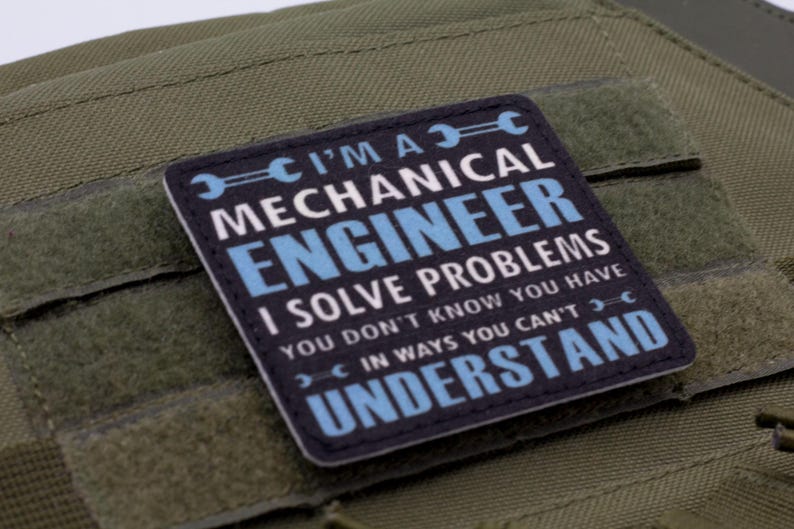 May include: A square patch with the text "I'M A MECHANICAL ENGINEER I SOLVE PROBLEMS YOU DON'T KNOW YOU HAVE IN WAYS YOU CAN'T UNDERSTAND" in white and blue on a black background. The patch is on a green fabric.